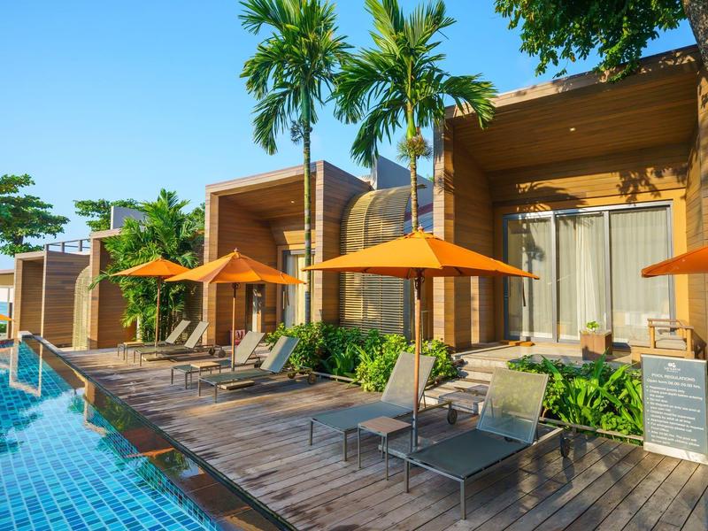 Moderner Poolbereich mit Liegestühlen, orangen Sonnenschirmen und Palmen an einer hölzernen Terrasse.