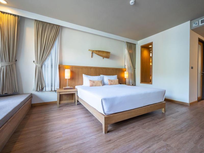 Helles Schlafzimmer mit Holzfußboden, Doppelbett, weißen Wänden, Fenstern mit Vorhängen und Nachttischen.