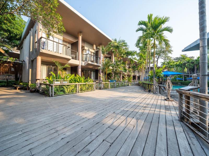 Großer Holzsteg mit Palmen vor modernen Hotelgebäuden unter klarem Himmel.