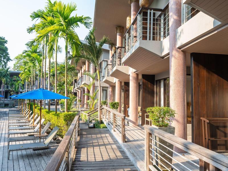 Moderner Balkon mit Metallgeländer, Holzboden und blauen Sonnenschirmen, umgeben von Palmen.