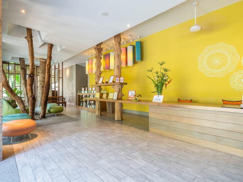 Ein heller, moderner Hotel-Empfangsbereich mit gelber Wand, Holztheke und entspannender Sitzecke.