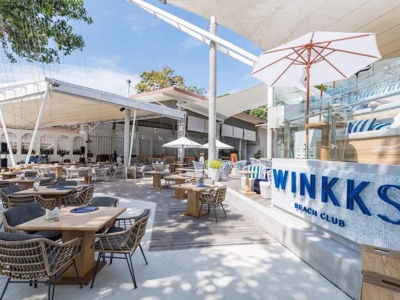 Große Terrasse mit Tischen, Stühlen und Sonnenschirmen neben modernem Gebäude bei Sonnenschein.