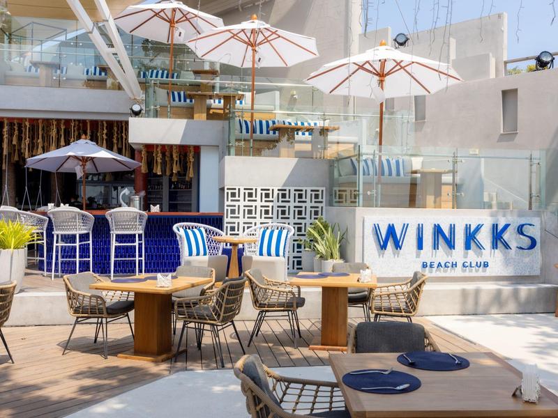 Moderner Außenbereich eines Cafés mit Holzmöbeln, blauen Akzenten und weißen Sonnenschirmen.