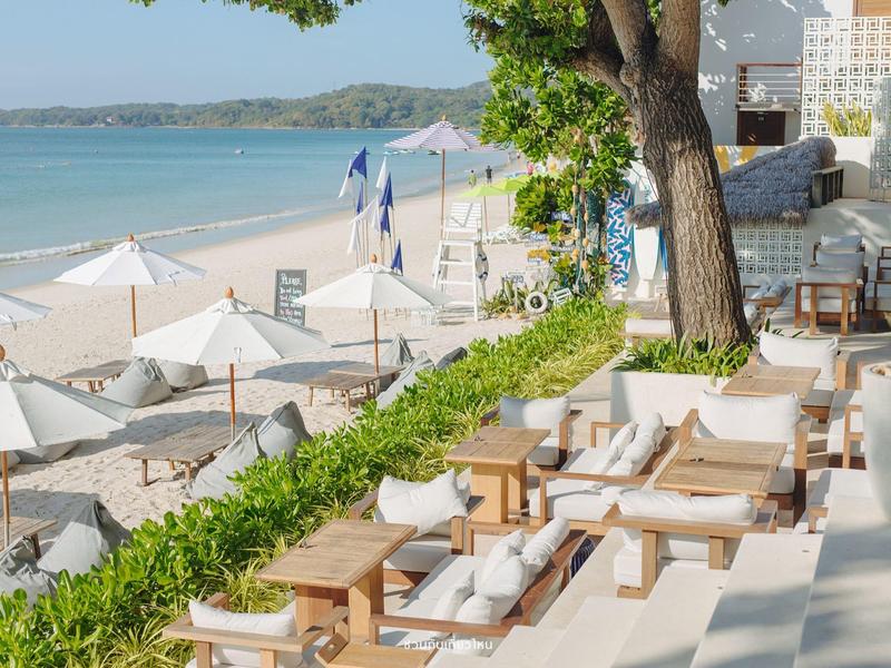 Strandhotel mit Liegestühlen, Sonnenschirmen und Blick auf das Meer bei sonnigem Wetter.