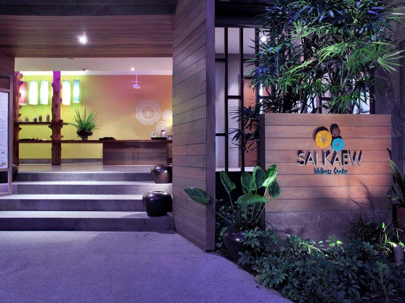 Moderner Gebäudeeingang mit Treppe, Holzverkleidung, Pflanzen und beleuchtetem "Saipaeu" Schriftzug.