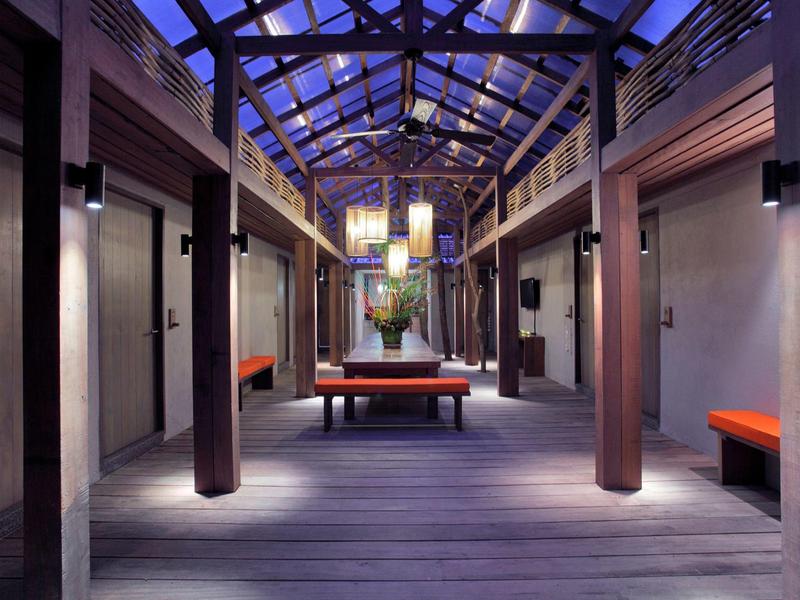 Langer heller Flur mit Holzboden, dunklen Holzbalken und orangen Sitzbänken an den Wänden.