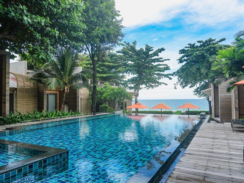 Modernes Hotel mit großem Pool, umgeben von grünen Bäumen und Blick aufs Meer.