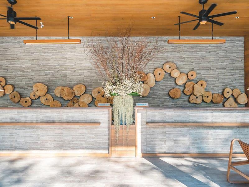 Moderner Empfangsbereich mit Holzscheiben-Dekor, Steintisch und großer Vase mit Zweigen.