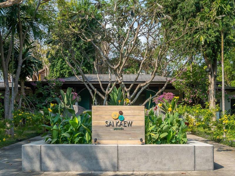 Eingang mit Schild und tropischem Garten, umgeben von Bäumen und Pflanzen.