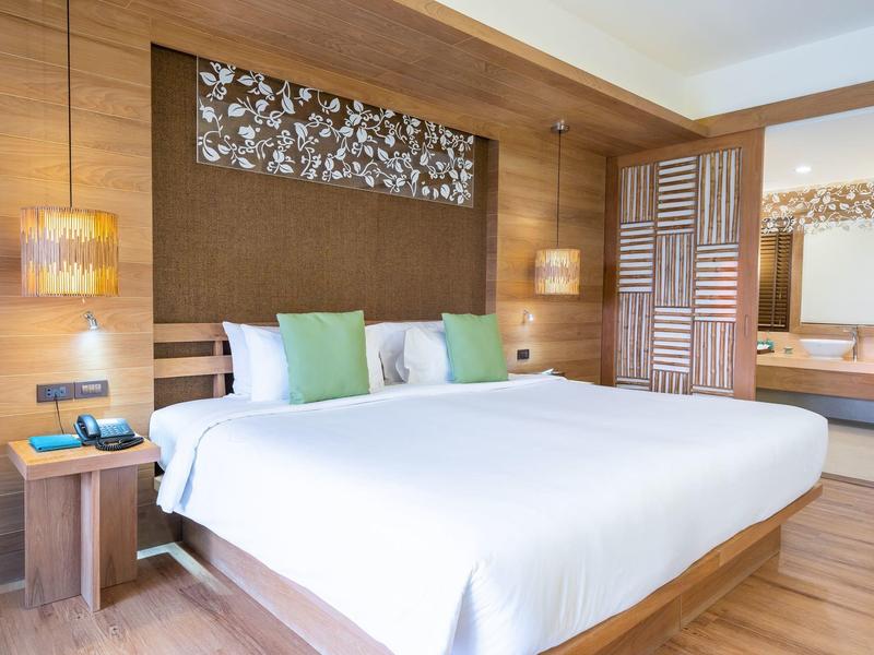 Modernes Schlafzimmer mit großem Bett, weißen Bettlaken, Holzwänden und grünen Kissen.