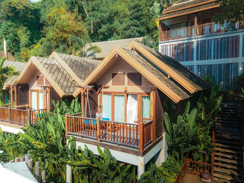 Zwei Holzhäuser mit großen Fenstern, Terrasse und umliegender grüner Vegetation.