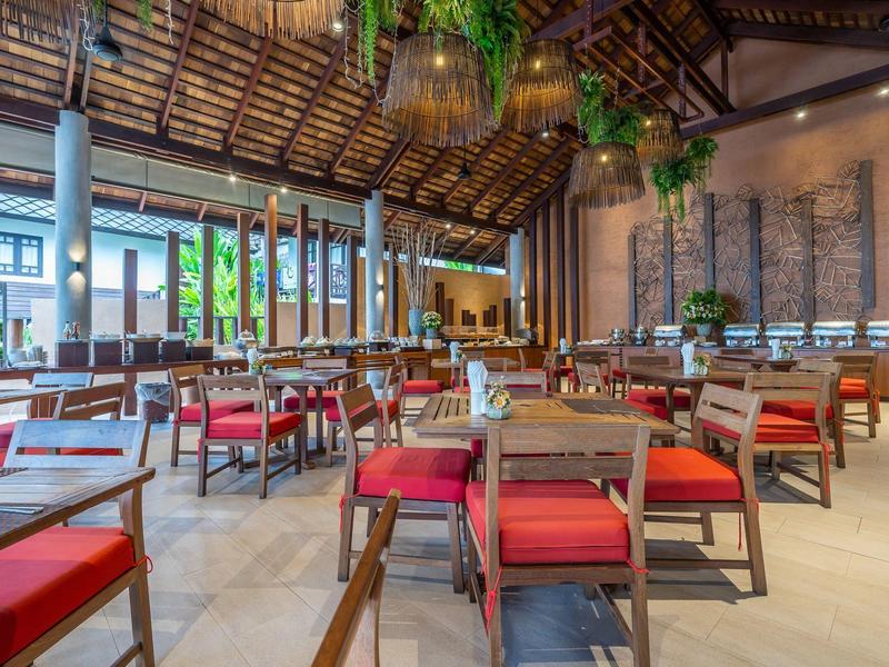 Großer offener Speisesaal mit Holzdach, roten Stühlen und grün hängenden Pflanzen.