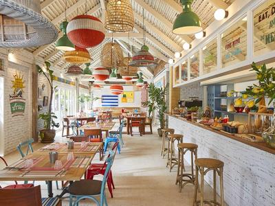 Hell eingerichtetes Café mit bunten Stühlen, Pflanzen und rustikalem Holzinterieur.