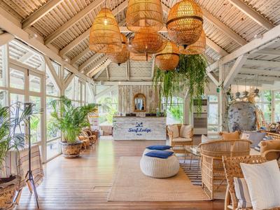 Helles, offenes Wohnzimmer mit Holzbalkendecke, Pflanzen und gemütlichen Korbmöbeln in Naturtönen.