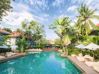 Une piscine d'hôtel tropicale avec des chaises longues et des arbres sous un ciel bleu.