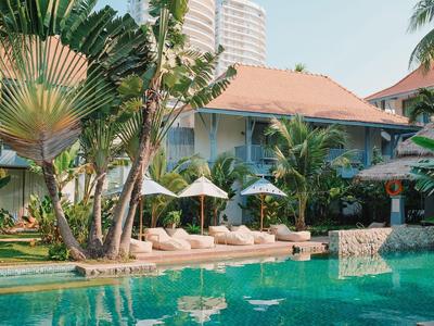 Piscine d'hôtel avec transats et parasols entourée de plantes tropicales et de bâtiments.