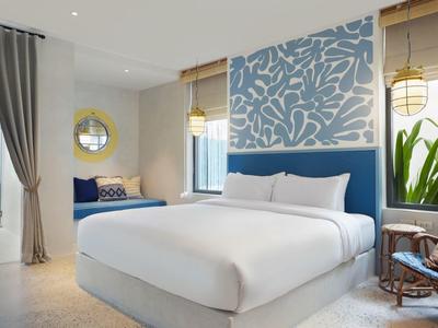 Schlafzimmer mit großem Bett, blauer Akzentwand, Fensterbank-Sitzplatz und Pflanzen neben Stuhl.