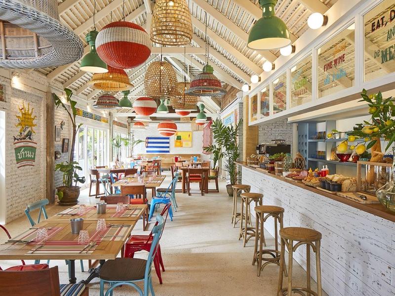 Hell eingerichtetes Café mit bunten Stühlen, Pflanzen und rustikalem Holzinterieur.