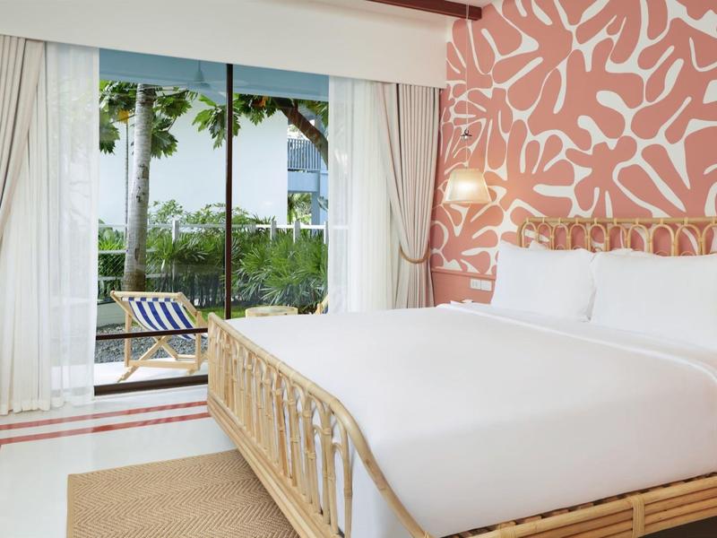 Helles Schlafzimmer mit großem Bett, roter Wand mit Muster, weißen Vorhängen und Blick auf Terrasse.