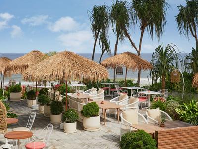 Espace extérieur d'hôtel avec parasols en paille, sièges et plantes vertes sous un ciel bleu.