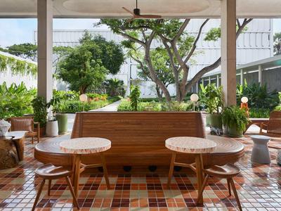 Helle Terrasse mit Fliesenboden, Holzmöbeln, Pflanzen und Blick auf grünen Garten und Himmel.