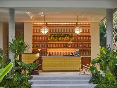 Espace bar d'hôtel moderne avec comptoir doré et plantes vertes luxuriantes.