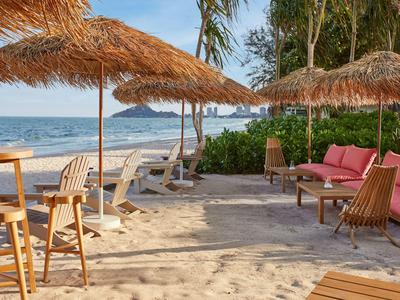 Bar de plage avec toits en paille, sièges et vue sur la mer sous un ciel clair.