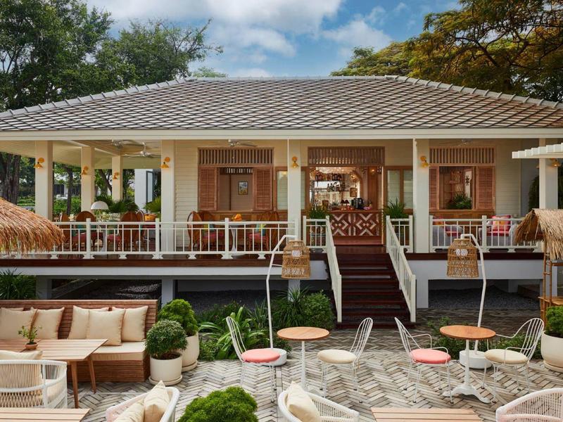 Großes, offenes Terrasse-Haus mit weißen Säulen, Holzdach, Treppe und Gartensitzplätzen.