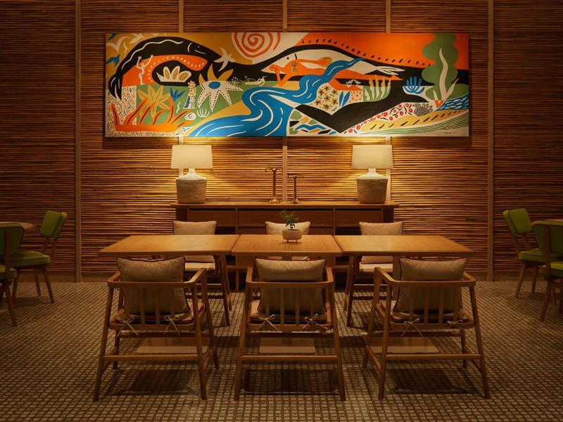 Gemütlicher Essbereich mit Holzmöbeln, Teppichboden und farbenfrohem Wandbild mit Flussmotiv.