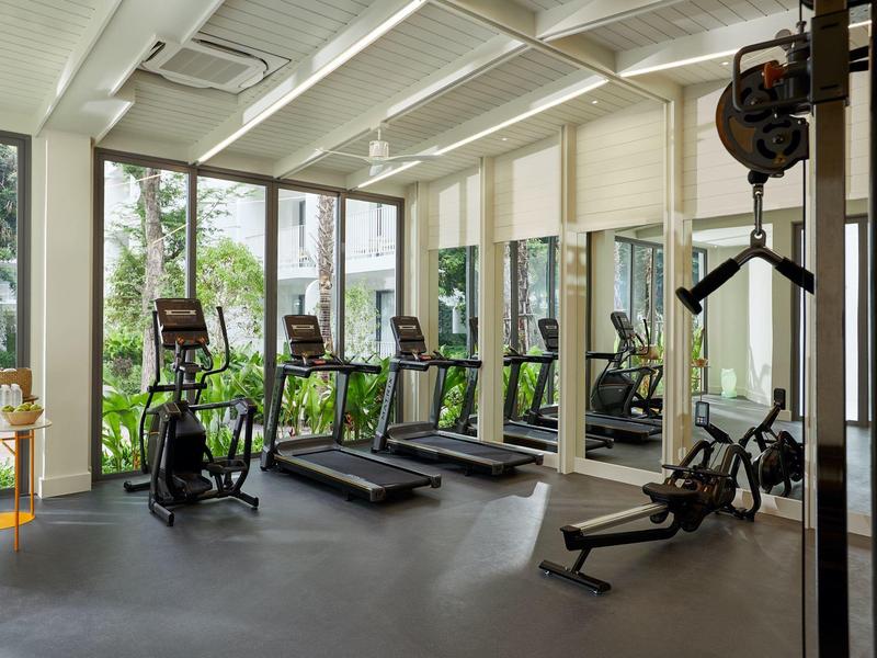 Hell eingerichteter Fitnessraum mit mehreren Laufbändern, Ergometern und großen Fenstern zum Garten hin.