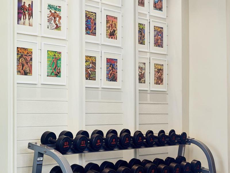 Dumbbell-Regal vor weißer Wand mit 18 bunten Comic-Postern in drei Reihen und vier Spalten.