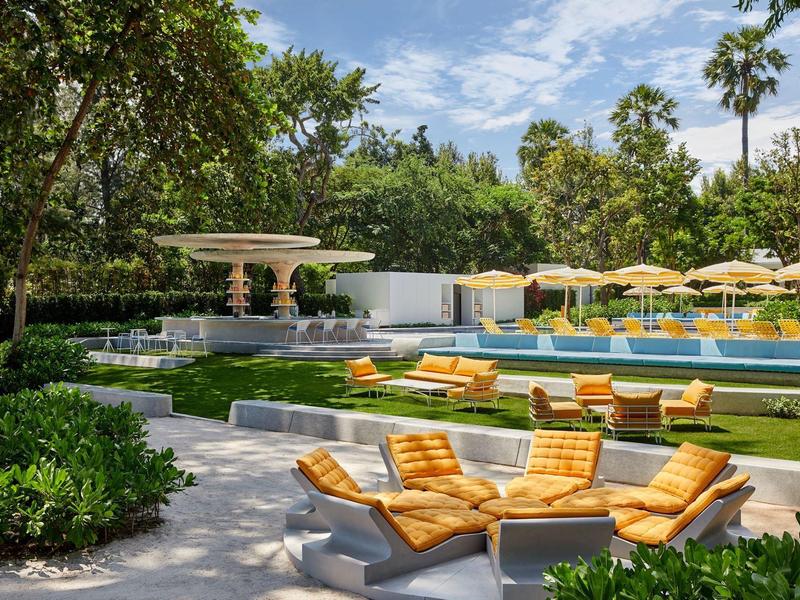 Moderner Außenpool mit gelben Liegen, Sonnenschirmen und umgeben von grünen Bäumen und Himmel.