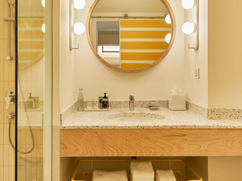 Modernes Badezimmer mit runden Spiegel, gelbem Handtuchhalter und weißen Handtüchern unter Waschbecken.