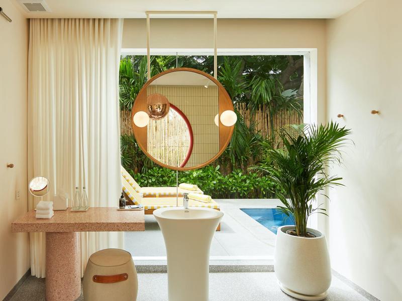 Heller Raum mit runder Spiegel, moderner Möbel, großer Pflanze und Blick auf Garten mit Swimmingpool.