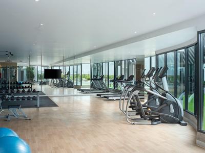 Gimnasio bien iluminado con equipo moderno y grandes ventanas con vista a una terraza.