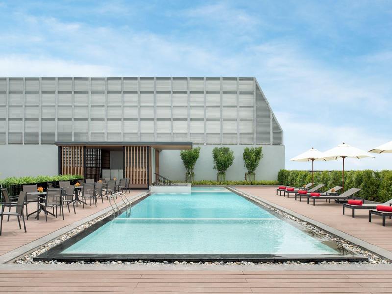 Piscine d'hôtel moderne sur une terrasse en bois avec chaises longues et tables sous un ciel bleu.