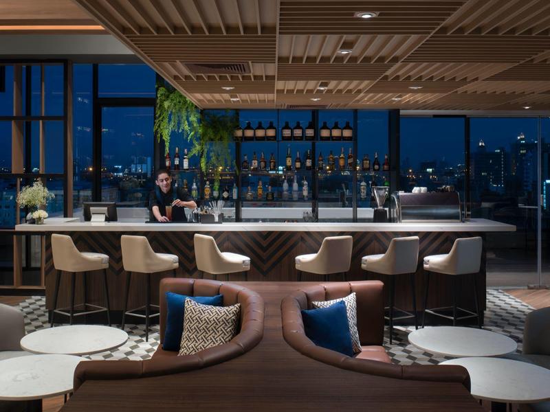 Bar d'hôtel moderne avec espaces assis, comptoir et vue nocturne sur la ville.