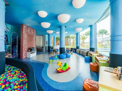 Espace de jeu pour enfants avec piscine à balles, jouets colorés et grandes fenêtres dans une pièce lumineuse.