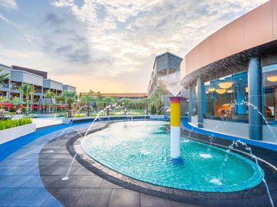 Piscine moderne de l'hôtel avec jeux d'eau et vue sur la station au coucher du soleil.