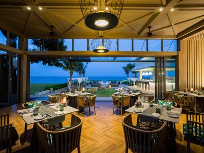 Restaurant ouvert avec vue sur la plage, ambiance du soir avec tables élégamment dressées et parquet en bois.