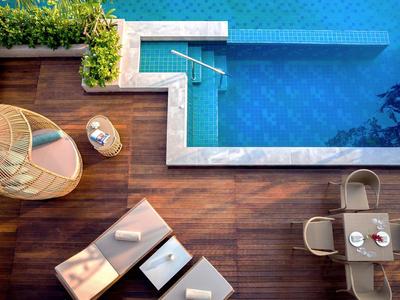 Vista aerea di una piscina con terrazza in legno, sdraio e tavolo da pranzo all'aperto.