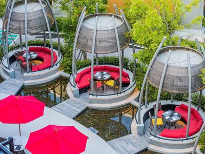 Áreas de asientos redondas modernas con cojines rojos sobre un estanque, rodeadas de plantas verdes.