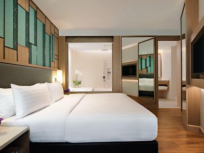 Chambre d'hôtel moderne avec grand lit, sol en bois et salle de bain adjacente.