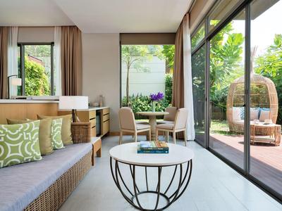 Salon lumineux avec canapé, coussins et table devant de grandes fenêtres donnant sur une terrasse avec sièges.