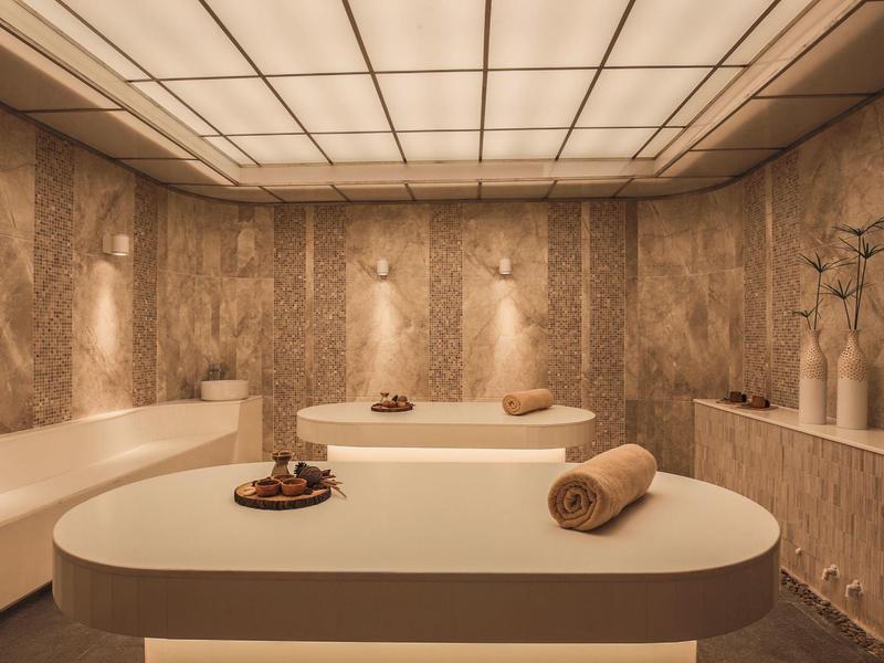 Salle de spa moderne avec tables de massage, serviettes et lumière chaude tamisée.