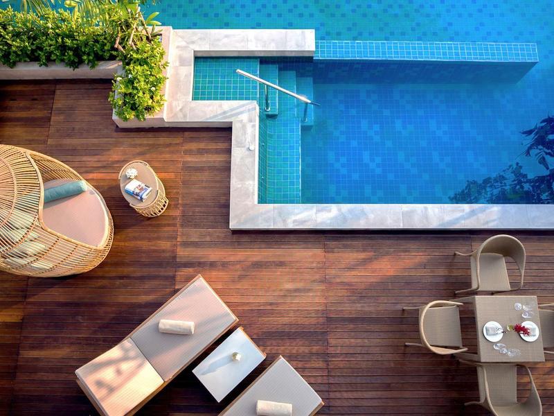 Vue aérienne d'une piscine avec terrasse en bois, chaises longues et table à manger extérieure.