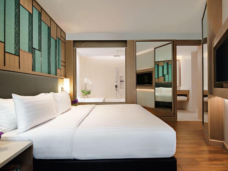 Chambre d'hôtel moderne avec grand lit, sol en bois et salle de bain adjacente.