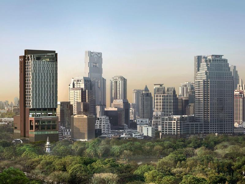 Urban skyline at sunset with modern skyscrapers and green park in the foreground.