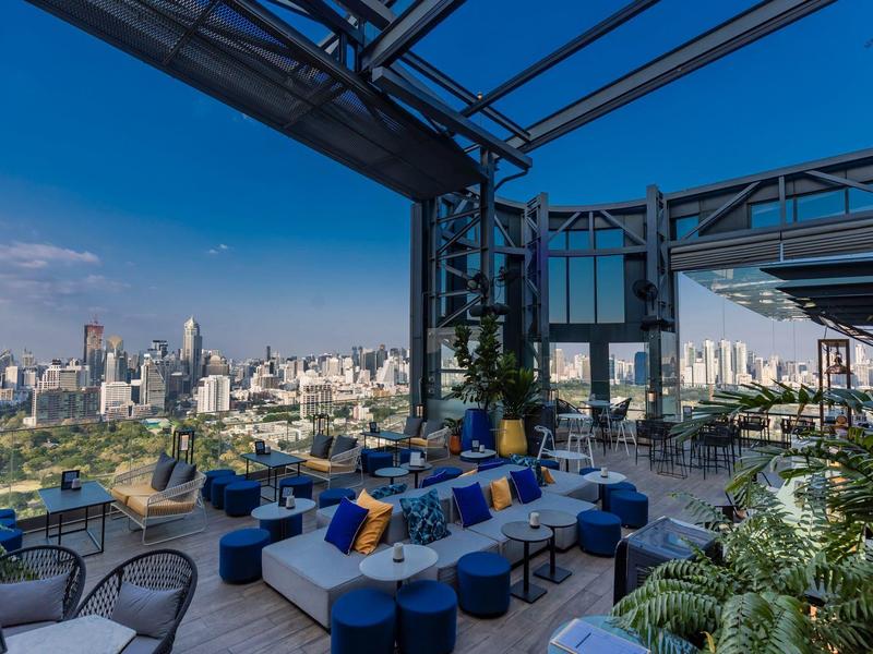 Rooftop terrace with seating, plants, and a city skyline with skyscrapers under clear sky.