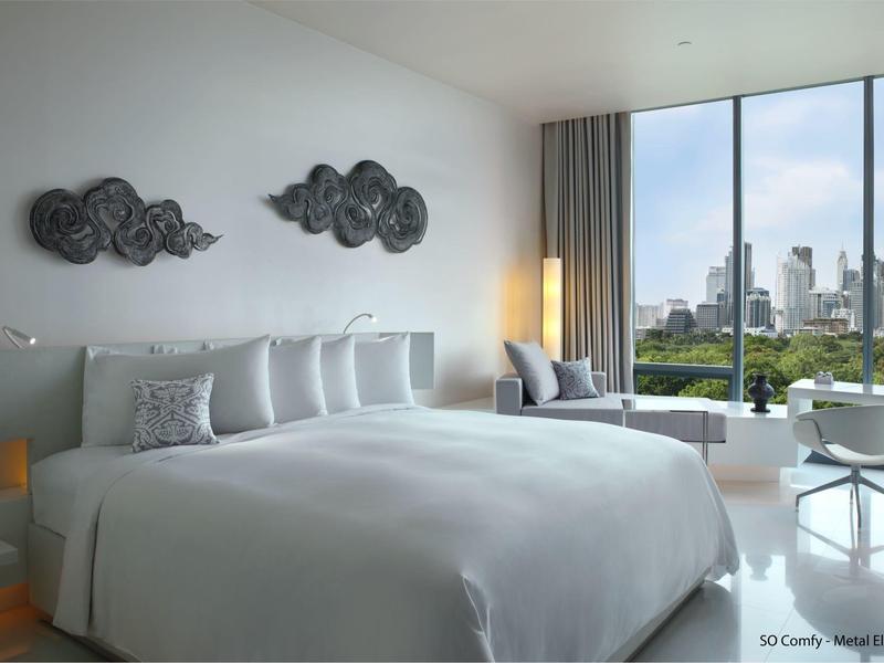 Modern hotel room with large bed, wall decoration, and large windows overlooking the city.
